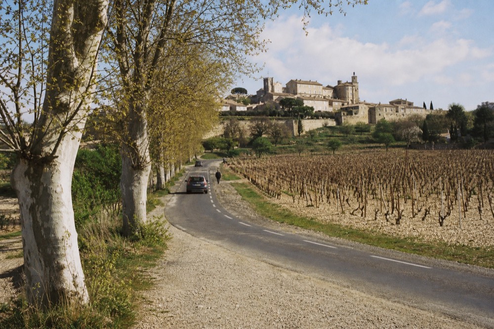 Country road winding through vineyards toward Châteauneuf-du-Pape on its hill, no text, no logos, no people.