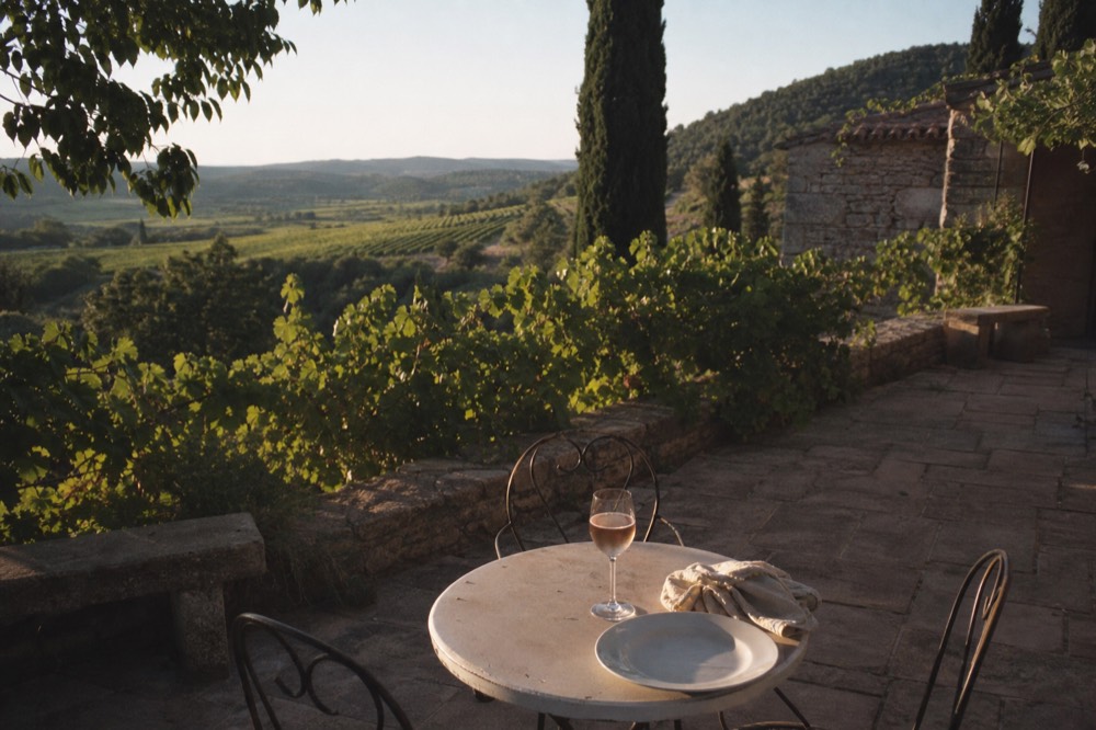 Outdoor dining terrace overlooking a vineyard with a glass of rosé, no text, no logos, no people
