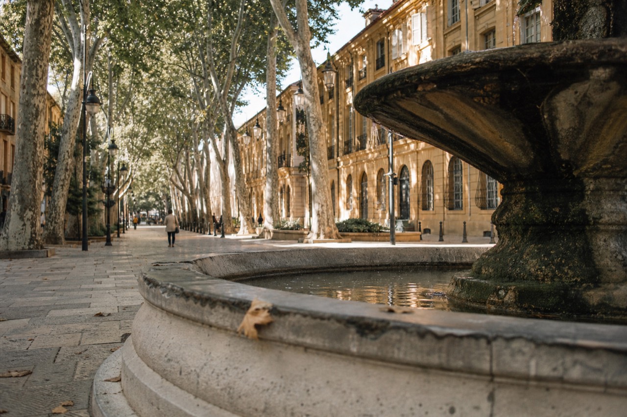 Sunlit limestone buildings and a tree-lined Cours Mirabeau in Aix-en-Provence, no text, no logos, no people.