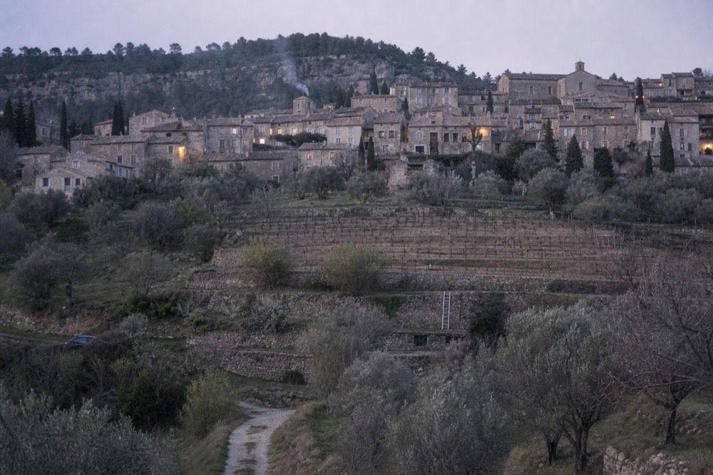 A perched stone village above vineyards and olive trees, no text, no logos, no people