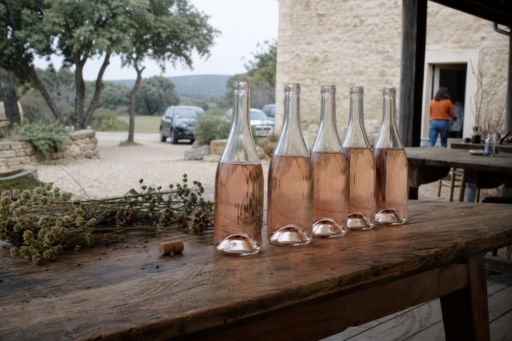 A row of pale rosé bottles on a wooden tasting-room table, no text, no logos, no people
