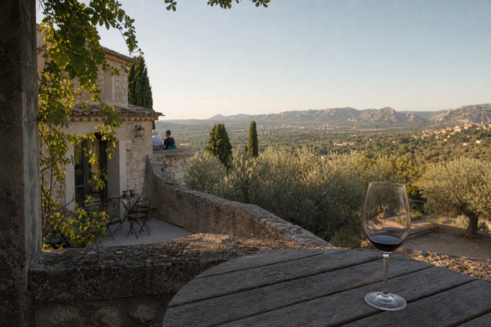 A glass of dark red wine on a stone terrace overlooking the Alpilles hills, no text, no logos, no people