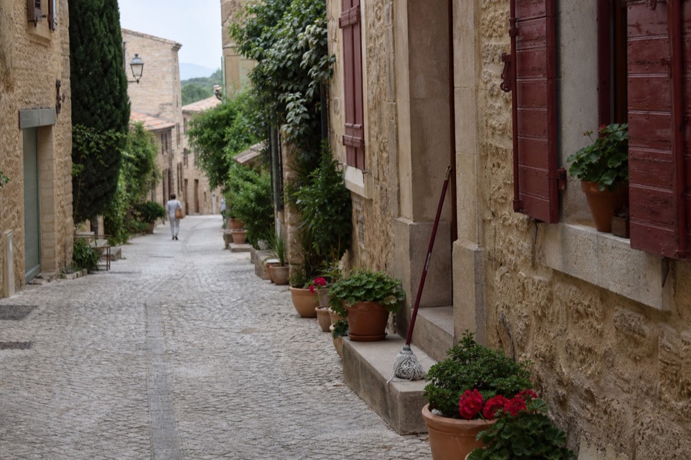 Luberon village street with stone walls and flowering pots, no text, no logos, no people