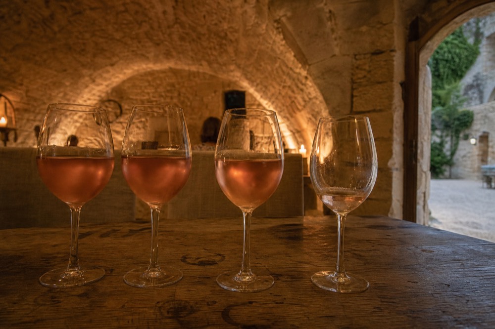 A tasting flight of rosé glasses on a wooden table in a vaulted cellar, no text, no logos, no people