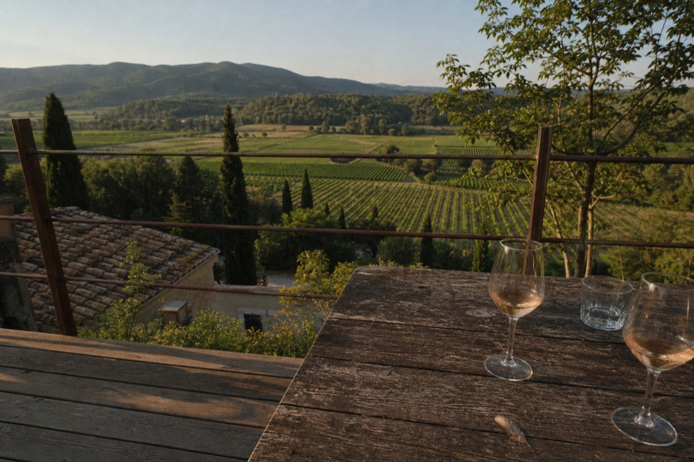 A tasting terrace with glasses of pale rosé on a wooden table overlooking a broad valley of vines, no text, no logos, no people