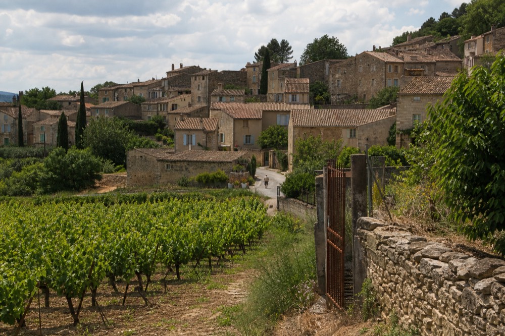 Stone village houses on a Luberon hillside surrounded by vines, no text, no logos, no people